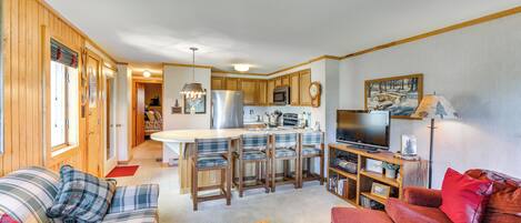 Un espacio habitable compacto con kitchenette, una zona de comedor con isla central y dos áreas de estar con sofás y sillones.