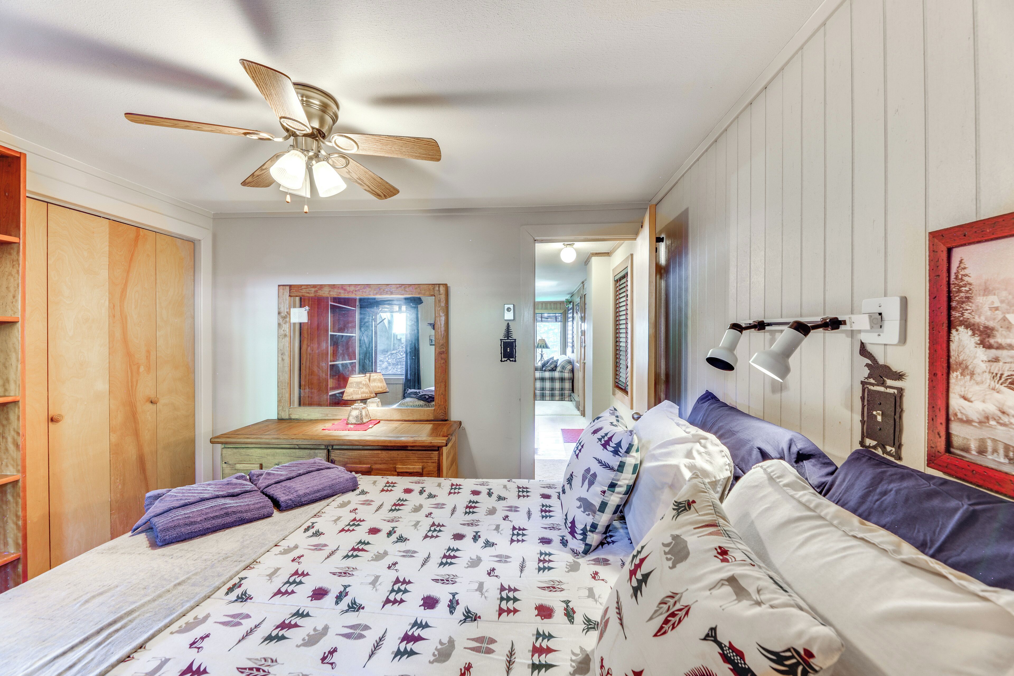 A bedroom with a bed, a ceiling fan, a dresser, a mirror, and a framed picture on the wall.