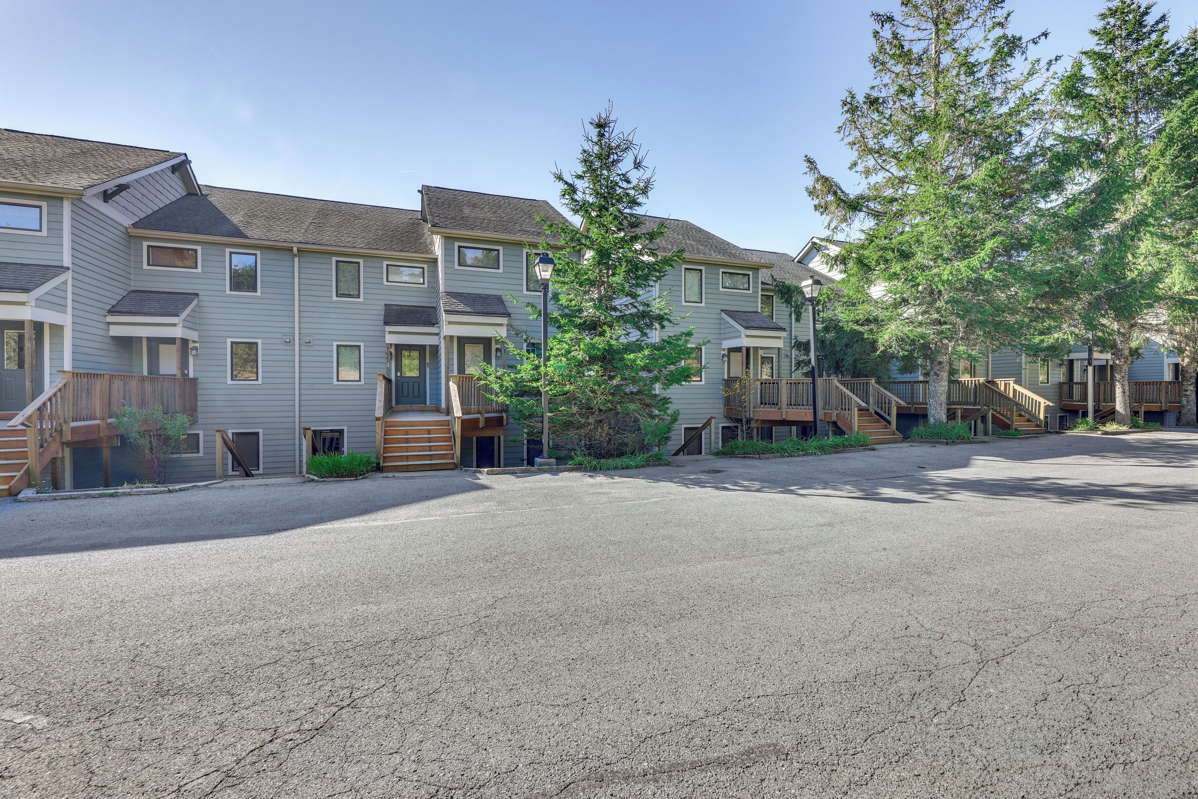 A row of townhouses with a gravel driveway, wooden stairs, and a small tree in the center.