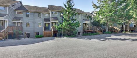 A row of townhouses with a gravel driveway, wooden stairs, and a small tree in the center.