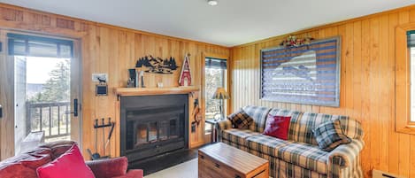 Una sala de estar acogedora con chimenea, sofá a cuadros, cojines rojos y paredes de madera.