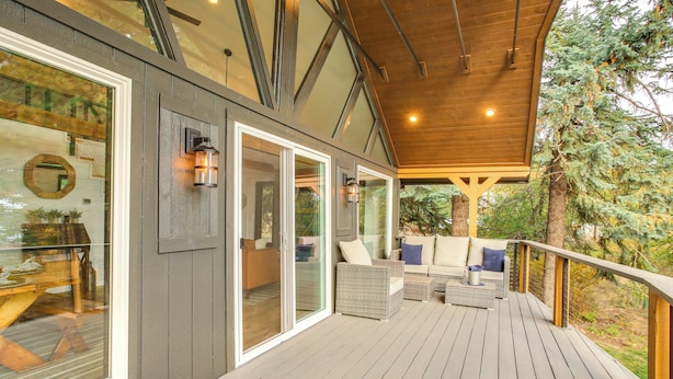 A covered deck with outdoor seating, large windows, and a wooden ceiling.