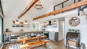 A spacious kitchen with wooden beams, a dining table with benches, and a rustic wooden sideboard.