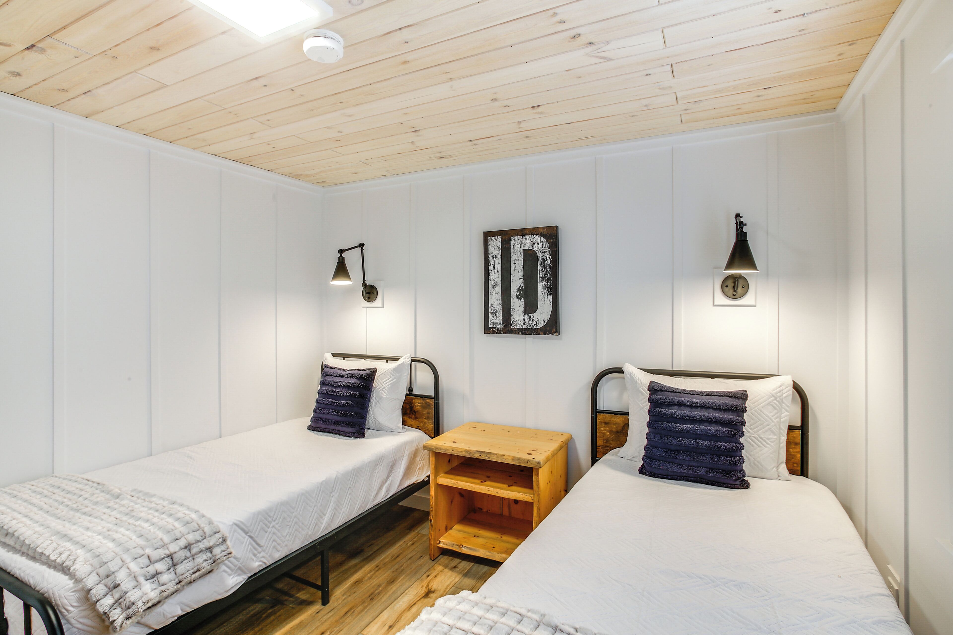 A room with two single beds, wooden flooring, white walls, and a wooden ceiling.