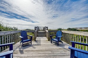 A wooden deck with two blue Adirondack chairs and a wooden staircase leading to a higher level. - Home on Ocean Isle Beach w/ Catwalk & Deck (Ocean Isle Beach)
