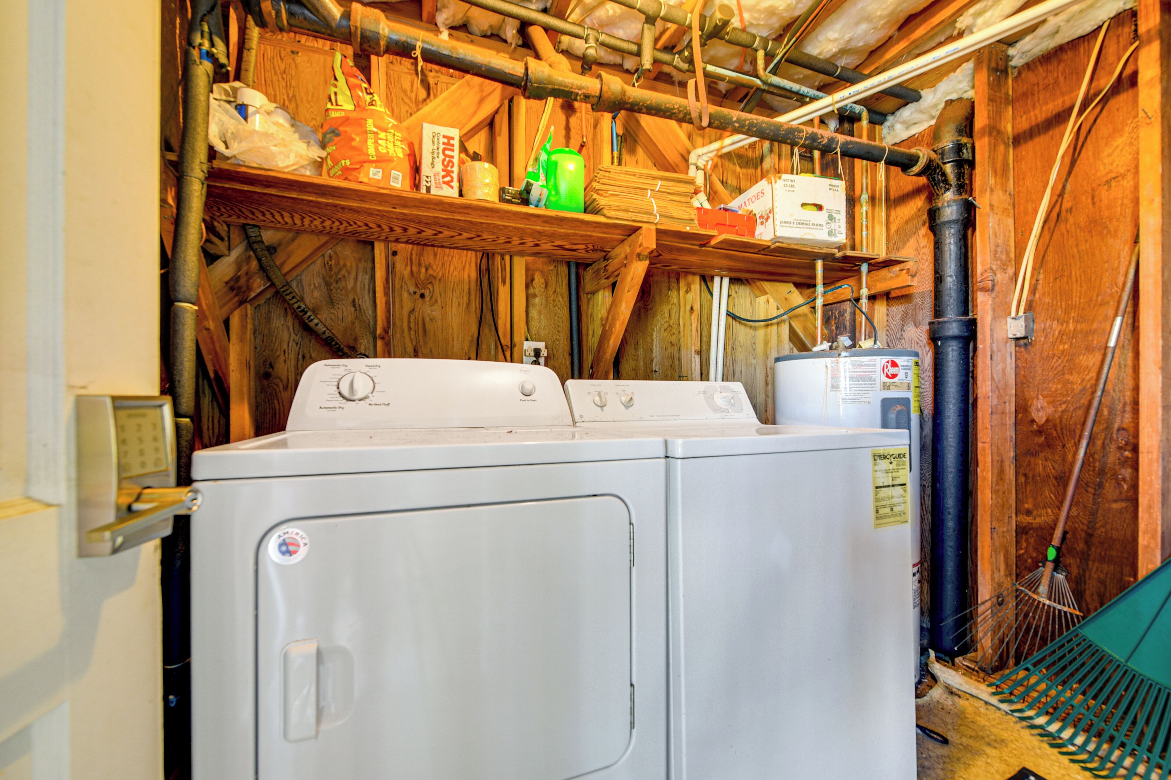 A laundry area with a washing machine, shelves with various items, and exposed wooden beams.