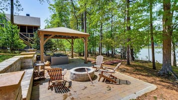 Un espacio de estar al aire libre techado con un brasero, sillas Adirondack y una chimenea de piedra.