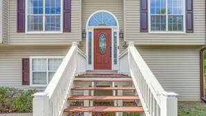 Une maison à deux étages avec une porte rouge, des balustrades blanches et un petit porche avec des marches menant à l’entrée.
