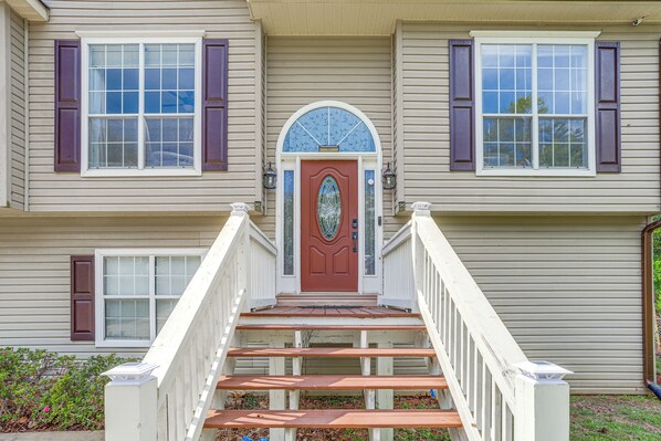 A two-story house with a red door, white railings, and a small porch with steps leading up to the entrance. - Lakefront Escape w/ Dock & Fire Pit: Sleeps 12 (Murrayville)