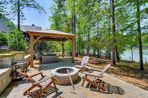 An outdoor patio with a fire pit, wooden chairs, and a covered seating area.