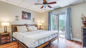 Une chambre à coucher avec un lit en bois, deux tables de chevet avec des lampes, un ventilateur de plafond et une grande fenêtre avec des rideaux.