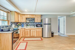 A modern kitchen with wooden cabinets, a stainless steel refrigerator, and a tiled backsplash. - Lake Champlain Fun: Apt w/ Fire Pit & Large Yard! (Essex Junction)