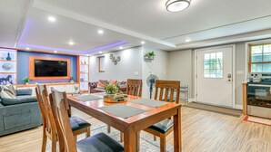 A modern living room with a wooden dining table, comfortable seating, a flat-screen TV, and decorative items. - Lake Champlain Fun: Apt w/ Fire Pit & Large Yard! (Essex Junction)