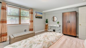 A bedroom with a bed, a bench, a desk, a wardrobe, and a window with curtains. - Lake Champlain Fun: Apt w/ Fire Pit & Large Yard! (Essex Junction)