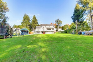 Enjoy a serene backyard with a large lawn, mature trees, and a play area featuring a swing set.
