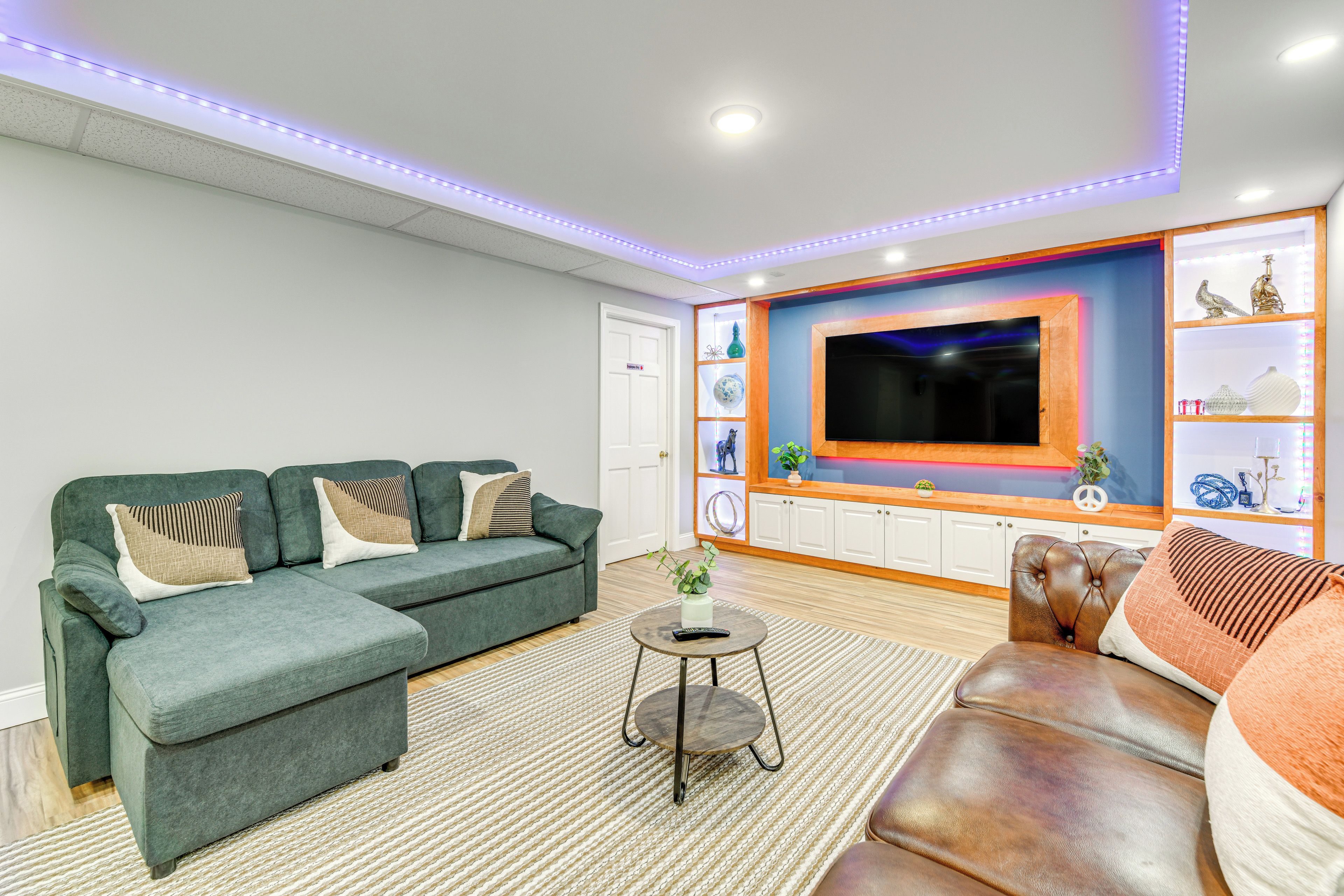 A modern living room with a sectional sofa, a leather armchair, a flat-screen TV, and a decorative shelf with various items.