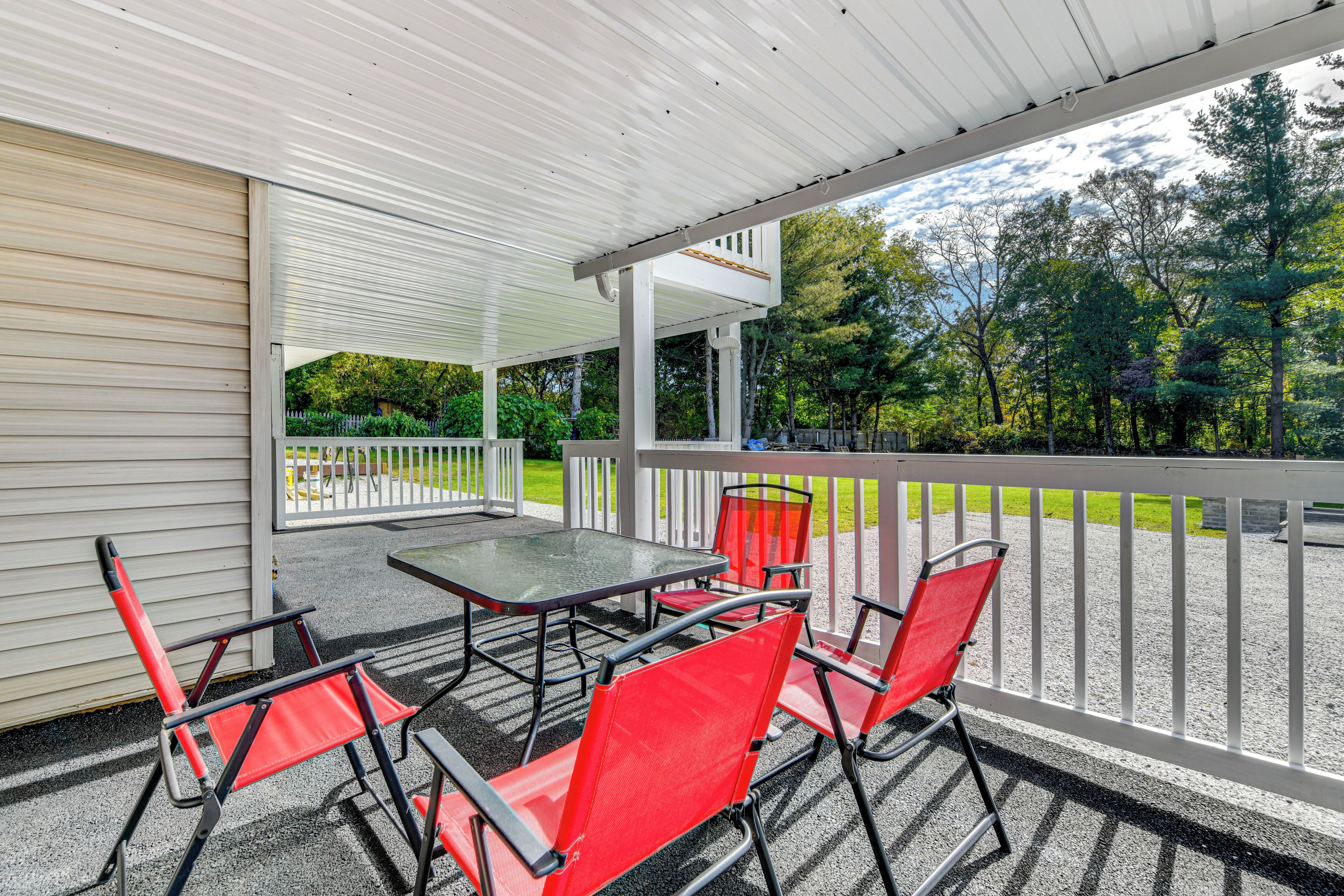 Une terrasse extérieure couverte, avec une table et des chaises rouges, donnant sur un espace verdoyant bordé d’arbres.