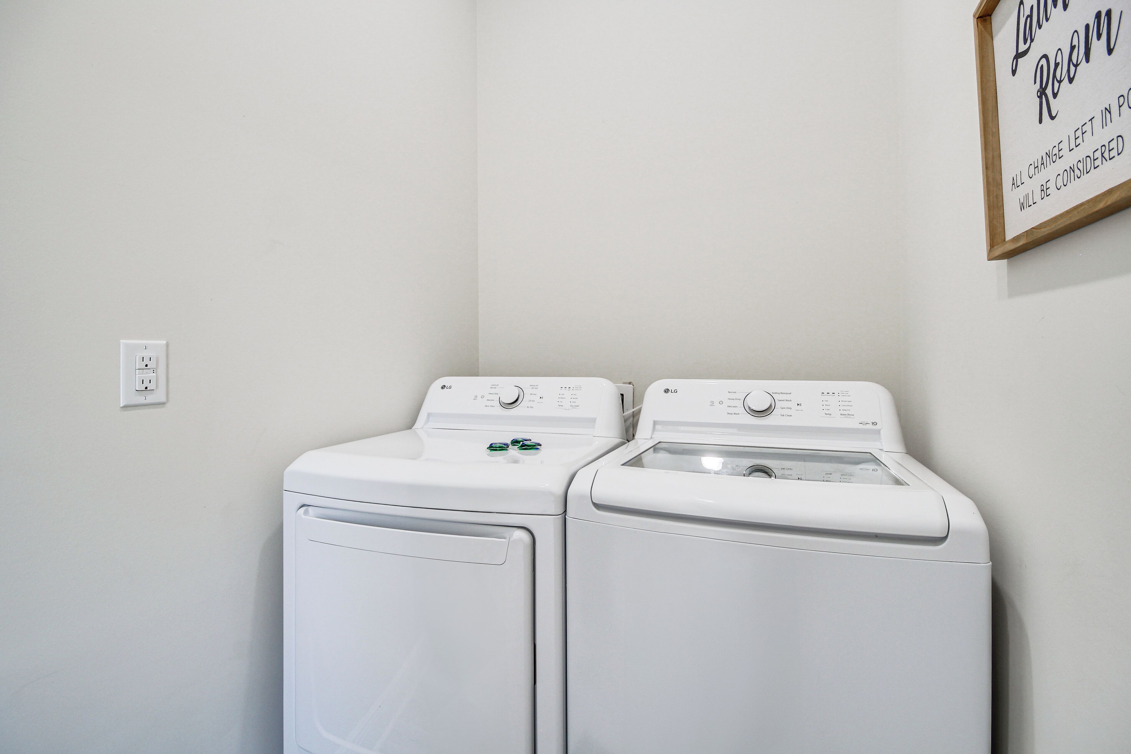 A laundry room with two white front-loading washing machines and a sign on the wall.