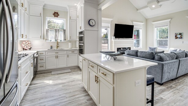 A modern kitchen with white cabinetry, a central island, and a gray sofa in the adjacent living area. - Steps to Beach: Modern Gulfport Getaway! (Gulfport)