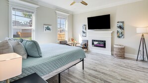 A bedroom with a bed, ceiling fan, TV, fireplace, and artwork. - Steps to Beach: Modern Gulfport Getaway! (Gulfport)