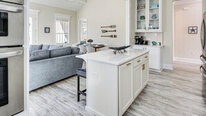 A modern kitchen with white cabinetry, a central island, and a dining area with a gray sofa. - Steps to Beach: Modern Gulfport Getaway! (Gulfport)