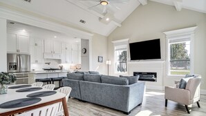 A spacious living area with a gray sectional sofa, a dining table with white chairs, and a fireplace. - Steps to Beach: Modern Gulfport Getaway! (Gulfport)