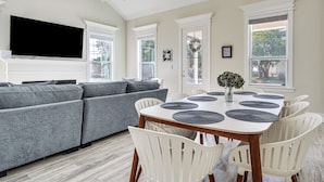 A modern living room with a grey sofa, a wooden dining table with white chairs, and a flat-screen TV mounted on the wall. - Steps to Beach: Modern Gulfport Getaway! (Gulfport)