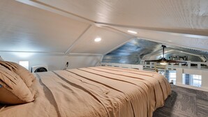 Una camera da letto con un letto grande, una ventola a soffitto e vista su un piano superiore con un balcone.