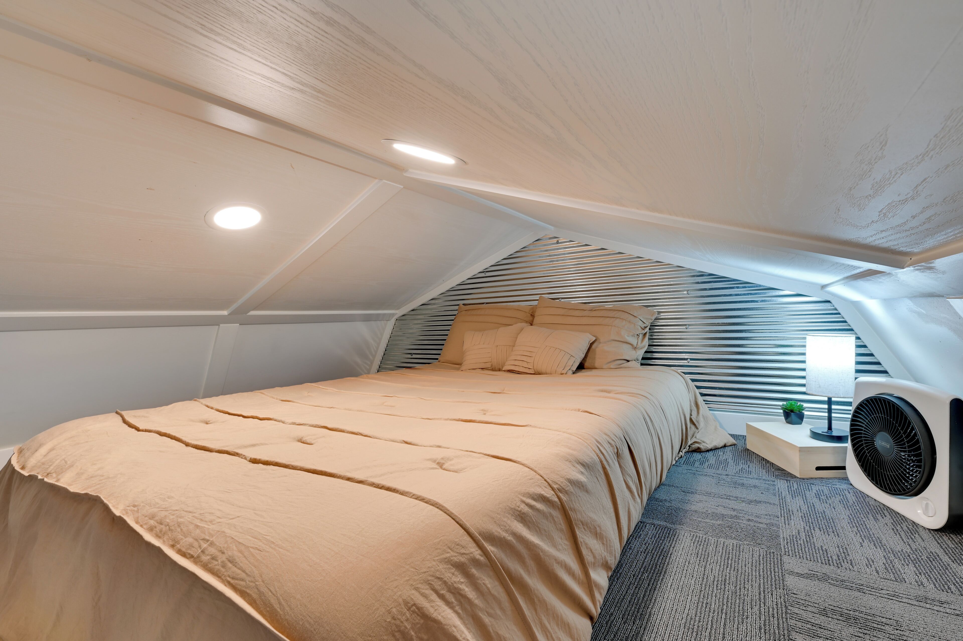 Ein Schlafzimmer mit einem Bett, einem Nachttisch, einer Lampe und einem Ventilator.