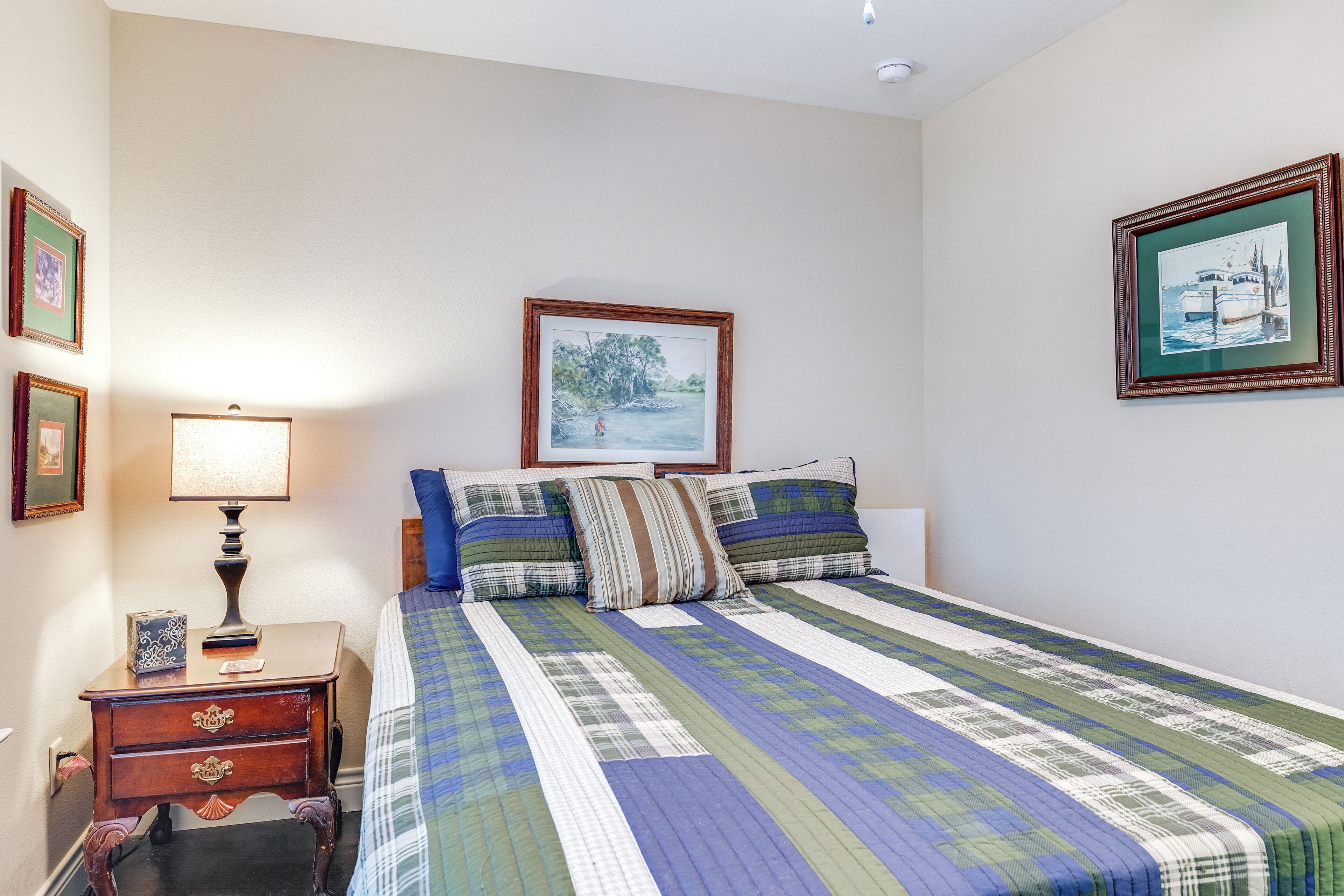 A neatly made bed with a striped bedspread, a bedside table with a lamp, and framed pictures on the walls.