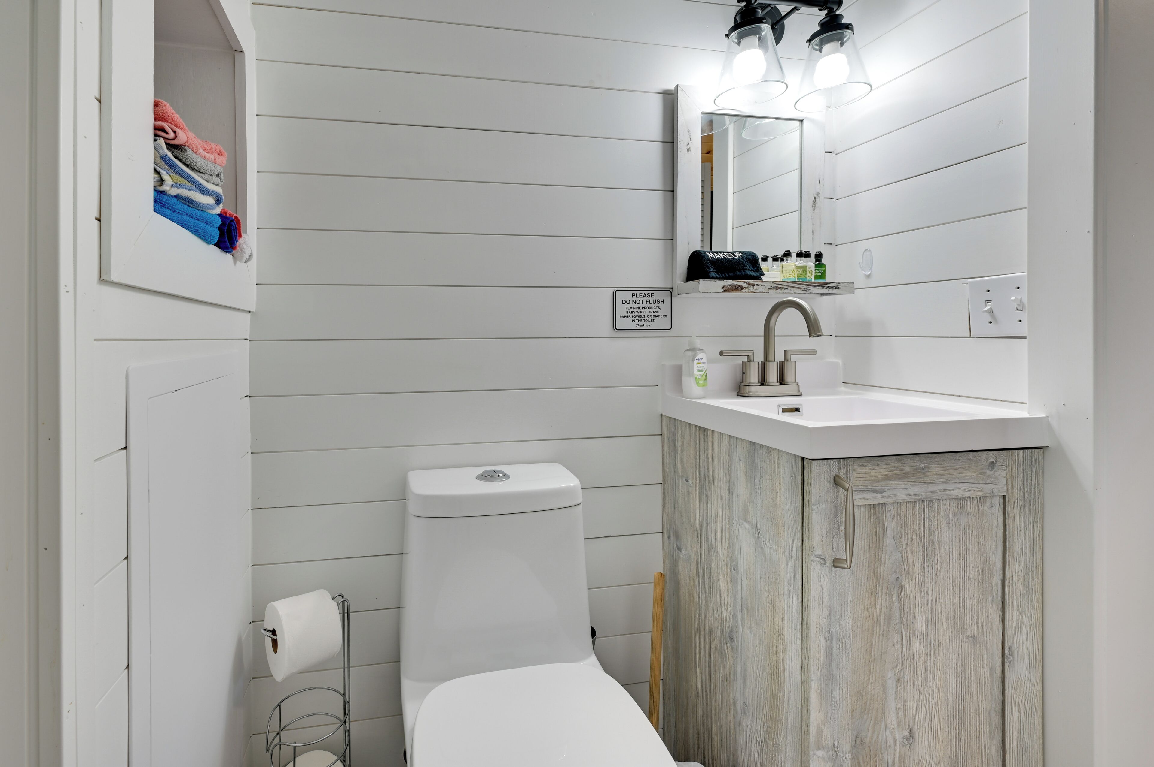 A bathroom with a white toilet, a sink with a mirror above it, and a towel rack with folded towels.