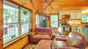 Un intérieur de chalet chaleureux avec un canapé en cuir, des murs en bois, un coin cuisine et de grandes fenêtres.
