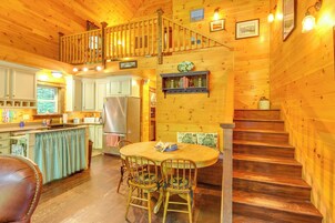 Interior de una cabaña de madera con comedor, cocina y una escalera.