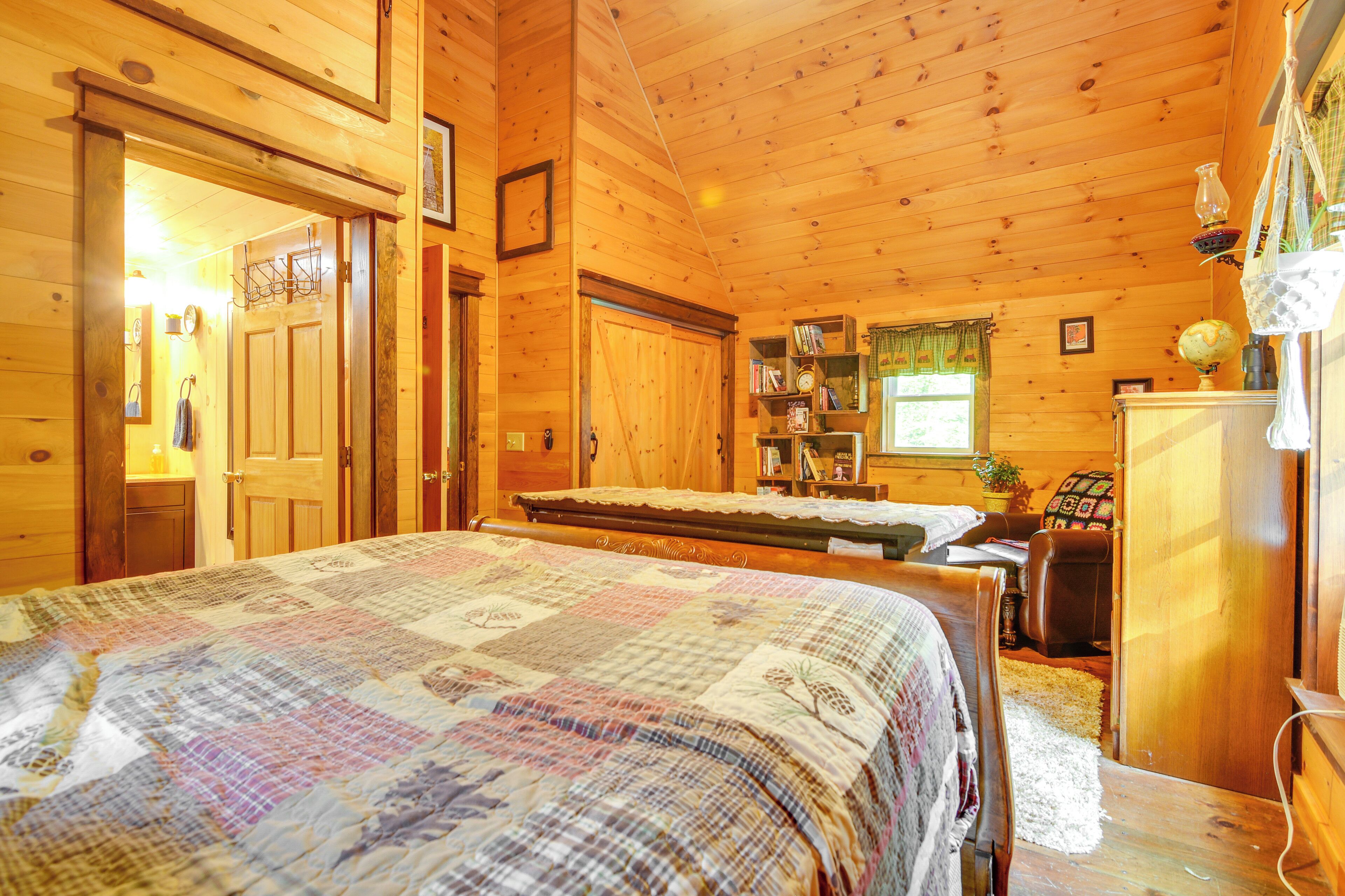 A wooden cabin bedroom with a quilted bedspread, a desk with a lamp, and a bookshelf.