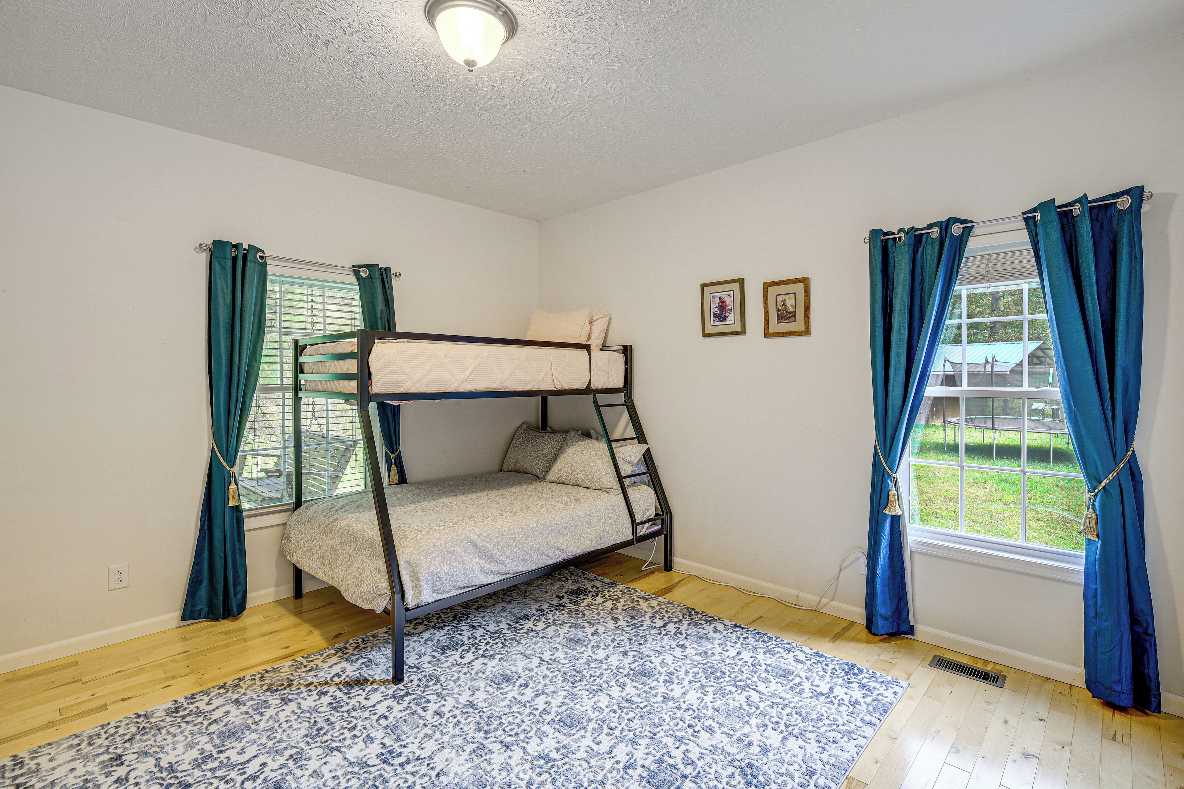 A bunk bed room with a patterned rug, two windows with curtains, and a ceiling light.