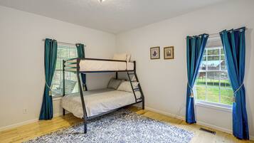 A bunk bed room with a patterned rug, two windows with curtains, and a ceiling light.