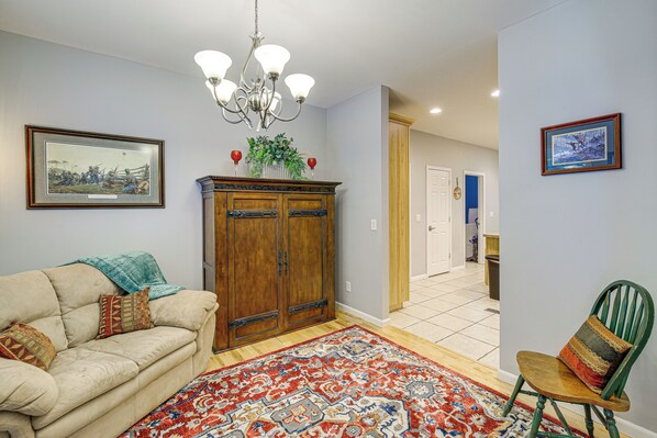 A living room with a beige sofa, a patterned rug, a wooden cabinet, and a green chair. - Breaks Home: 3 Mi to ATV Trails! (Breaks)