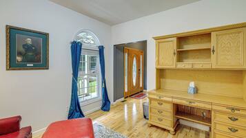 A room with a wooden desk, a red leather chair, a framed portrait, and a window with blue curtains.