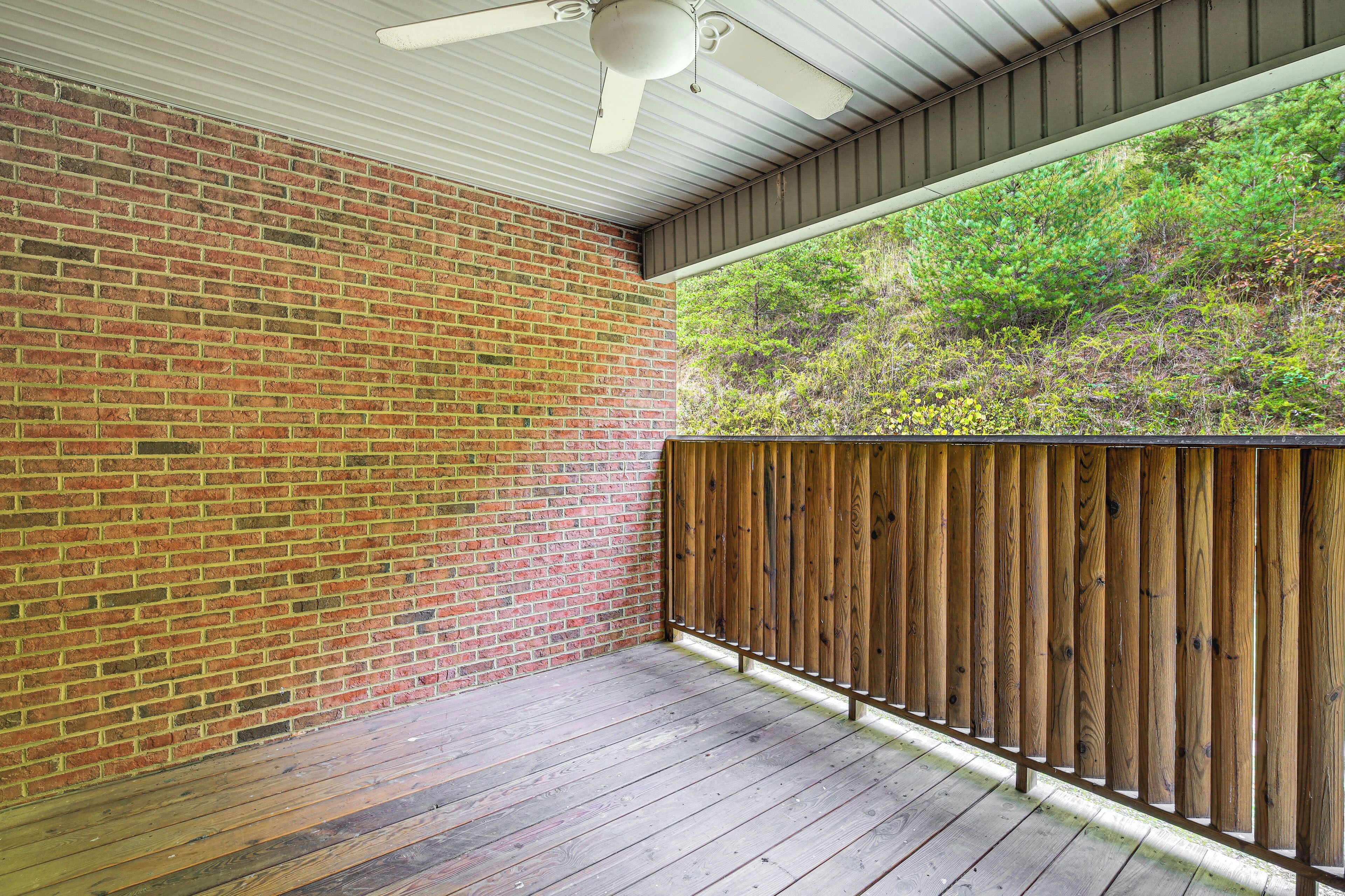 Un patio couvert avec un mur en briques, une clôture en bois et un ventilateur de plafond.