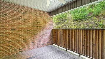 Un patio couvert avec un mur en briques, une clôture en bois et un ventilateur de plafond.