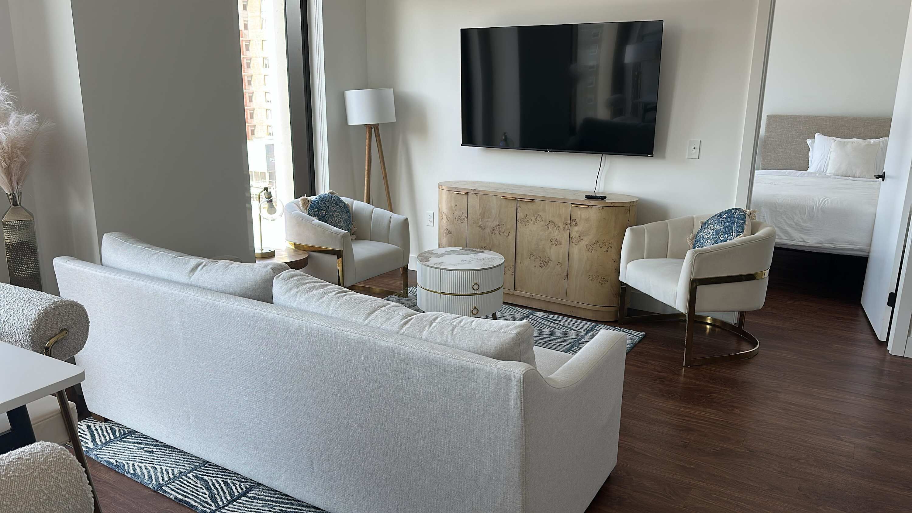 Un salon moderne comprenant un canapé, deux fauteuils, une petite table ronde, un meuble en bois et un téléviseur à écran plat.