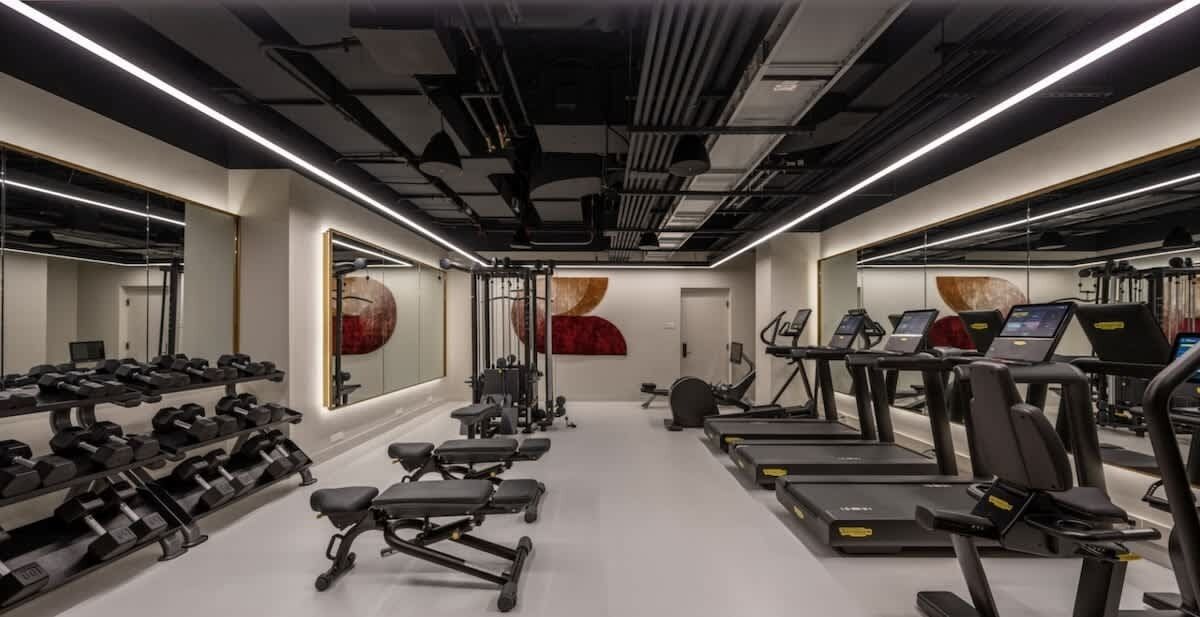 Une salle de sport moderne équipée de tapis de course, de vélos elliptiques et de poids libres.