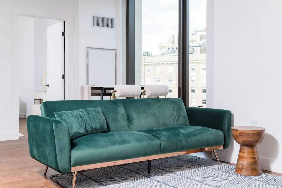 A modern living room with a green sofa, a wooden side table, and a patterned rug.