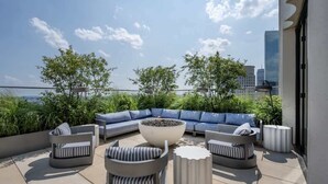 Terraço no telhado com um sofá de canto, uma mesa de centro redonda e um espaço de estar com cadeiras e mesinhas.