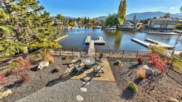 A lakeside patio with a fire pit, seating, and a view of the lake and surrounding buildings. - Luxury Keys Living: 3BR, Pool, Boat Dock, & BBQ (South Lake Tahoe)