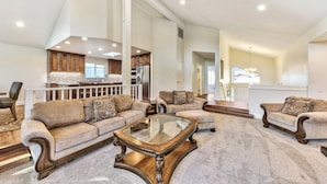 A spacious living area with a high ceiling, a glass coffee table, and a kitchen in the background. - Luxury Keys Living: 3BR, Pool, Boat Dock, & BBQ (South Lake Tahoe)