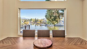 A dining area with a large window overlooking a river and boats, three chairs, and a wooden table. - Luxury Keys Living: 3BR, Pool, Boat Dock, & BBQ (South Lake Tahoe)
