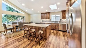 A modern kitchen with wooden cabinets, a stainless steel refrigerator, and a dining area with a large island and chairs. - Luxury Keys Living: 3BR, Pool, Boat Dock, & BBQ (South Lake Tahoe)