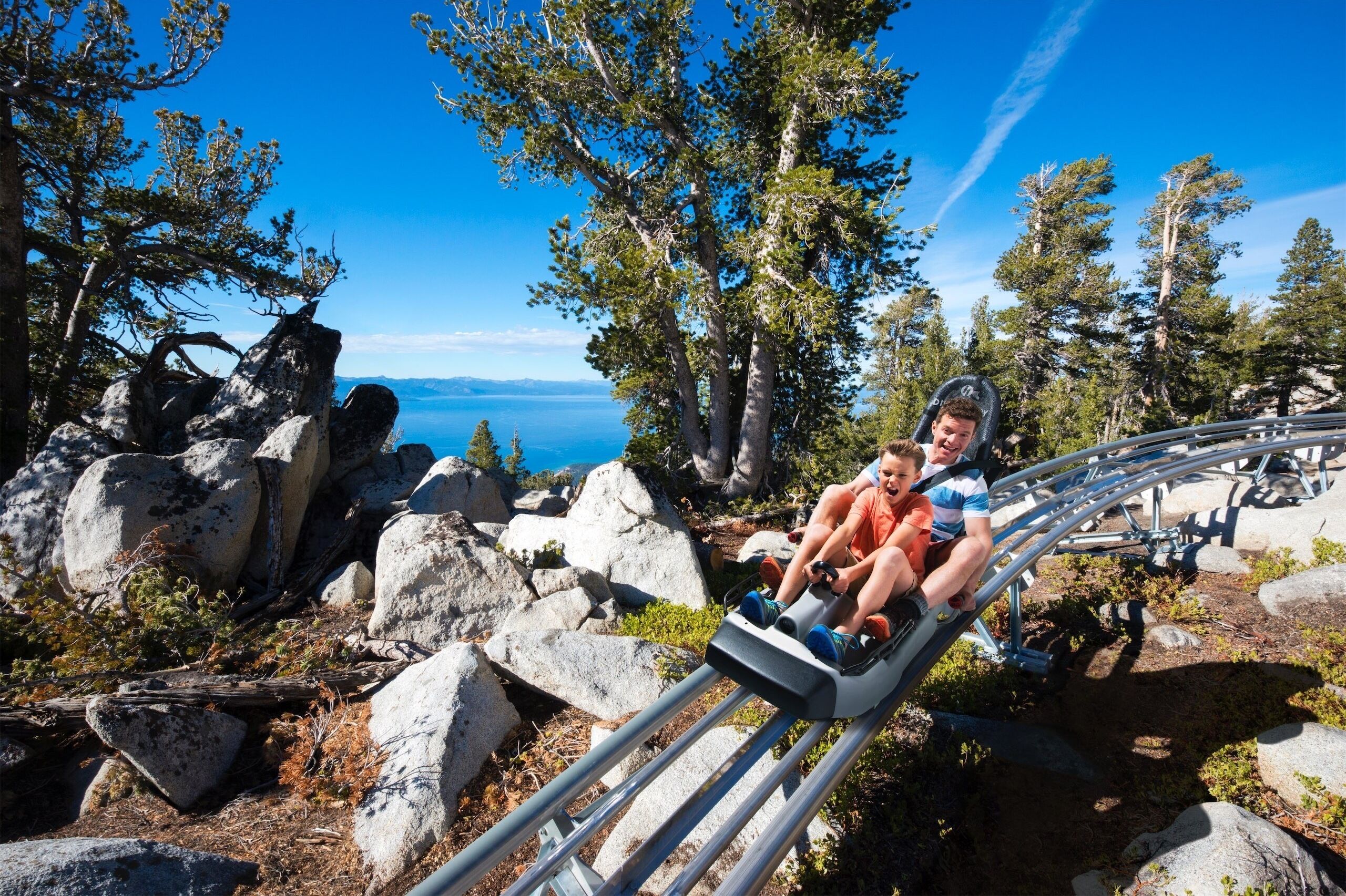 A person on a chairlift in a mountainous area with rocky terrain and trees.