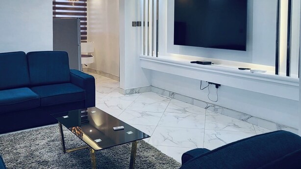 Una sala de estar moderna con un televisor de pantalla plana grande montado en la pared, un sofá azul, una mesa de centro y un ventilador de techo.